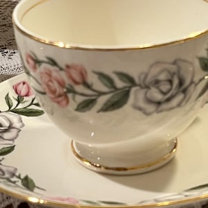 Peut inclure: Service à thé crème avec une décoration florale de roses roses et grises, bordée d'or. La tasse à thé a un piedestal et une anse incurvée. La soucoupe reprend le motif de la tasse.