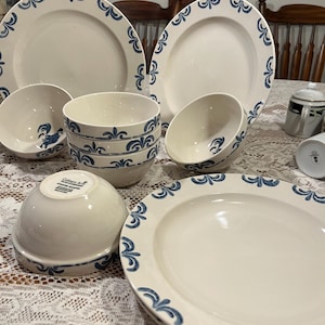 Könnte beinhalten: Eine Sammlung weißer Keramik-Geschirr mit blauem Blumendesign. Das Set umfasst Teller und Schalen in verschiedenen Größen. Die Teller und Schalen haben einen blauen Blumenrand. Das Geschirr ist auf einer weißen Spitzentischdecke angeordnet.