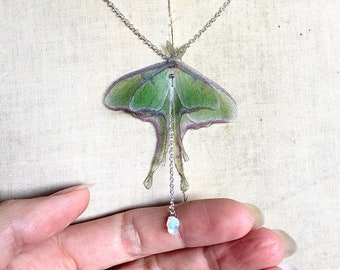 May include: A silver chain necklace featuring a green and white moth pendant with a small iridescent opal stone at the end.