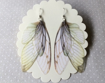 Peut inclure: Une paire de boucles d'oreilles avec de délicates ailes translucides à motifs verts et blancs. Les ailes sont attachées à des crochets argentés.