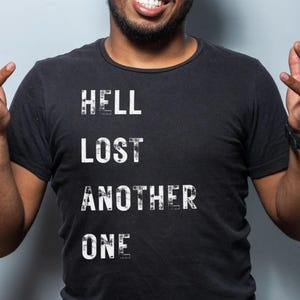 Puede incluir: Una camiseta negra con texto blanco que dice "HELL LOST ANOTHER ONE".