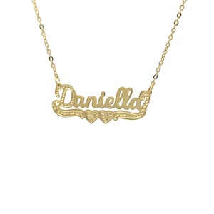 May include: Gold necklace featuring the name "Daniella" in a cursive script with two small hearts on either side of the name.