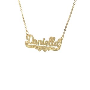 May include: Gold necklace featuring the name "Daniella" in a cursive script with two small hearts either side.