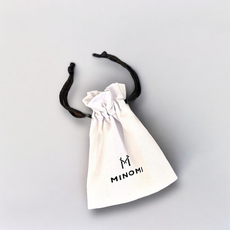 May include: White drawstring pouch with black drawstrings and the text "MINOMI" and a stylised "M" logo.