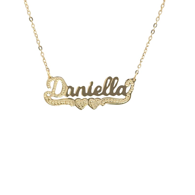 May include: Gold necklace featuring the name "Daniella" in a cursive script with two small hearts flanking the name.