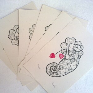 Puede incluir: Un conjunto de 7 tarjetas en blanco con una ilustraci&oacute;n en blanco y negro de un camale&oacute;n con corazones rojos en una cuerda. La tarjeta est&aacute; numerada 41/100 y firmada "Arie" en tinta negra.