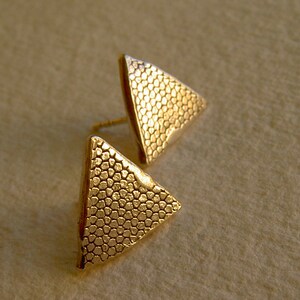 May include: A pair of gold triangle earrings with a textured surface.