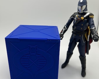May include: A blue box with a Cobra logo on the front. The box is about the size of a small action figure. The action figure is standing next to the box.