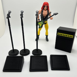 May include: A rock and roll action figure with a guitar, microphone stands, and an amplifier. The figure has red hair, a black vest, and yellow pants. The guitar is green and black. The amplifier is black with yellow accents.