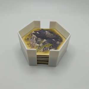 May include: A white, hexagonal card holder filled with landscape-themed cards. The cards feature a detailed illustration of a mountain range and surrounding terrain. The holder is made of a smooth, opaque material.