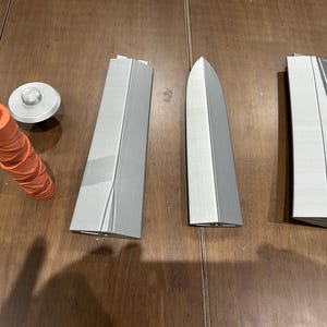 May include: A collection of 3D-printed parts. There's an orange, textured cylinder, a silver disc, and several grey, angular components. These could be elements of a larger model or project.