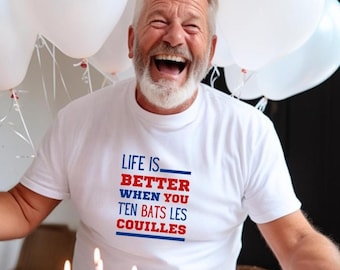 Może przedstawiać: Biała koszulka z napisem "LIFE IS BETTER WHEN YOU TEN BATS LES COUILLES" w kolorze czerwonym i niebieskim. Zdjęcie przedstawia osobę uśmiechniętą i śmiejącą się, z białymi balonami w tle.
