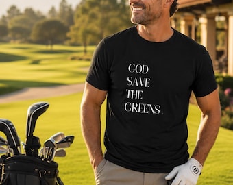 Może przedstawiać: Czarny t-shirt z białym napisem "GOD SAVE THE GREENS". Osoba ma na sobie czarną czapkę, spodnie khaki i białą rękawicę golfową. Torba golfowa z kijami jest widoczna na polu golfowym.