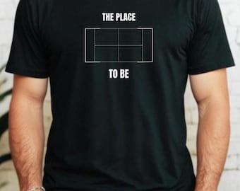 Może przedstawiać: Czarny t-shirt z napisem "THE PLACE TO BE" nad białym graficznym przedstawieniem kortu tenisowego. Koszulka jest z krótkim rękawem. Osoba nosząca koszulkę ma ręce w kieszeniach.