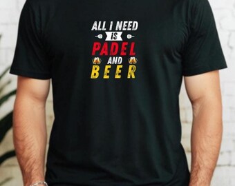 Może przedstawiać: Czarna koszulka z napisem "ALL I NEED IS PADEL AND BEER" w kolorze białym, czerwonym i żółtym. Koszulka zawiera grafikę rakiety do padla i kufli piwa. Osoba ma na sobie niebieskie dżinsy i zegarek.