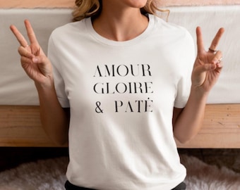 Może przedstawiać: Biały t-shirt z okrągłym dekoltem z czarnym napisem "AMOUR GLOIRE & PÂTÉ". Koszulka wykonana jest z miękkiego materiału i nadaje się do noszenia na co dzień.