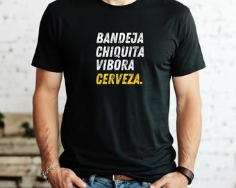 Może przedstawiać: Czarny t-shirt z białym i żółtym tekstem. Tekst brzmi "BANDEJA CHIQUITA VIBORA CERVEZA." Koszulka ma okrągły dekolt i jest noszona przez osobę.