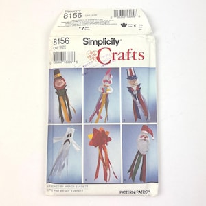 May include: Simplicity Crafts pattern 8156, featuring six whimsical craft designs. The designs include a scarecrow, clown, Uncle Sam, ghost, flower, and Santa Claus. The pattern is one size.