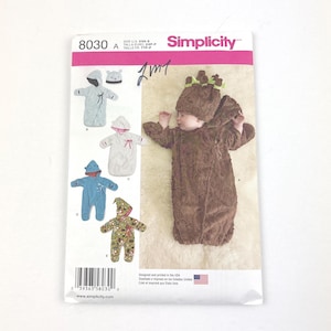 May include: Simplicity sewing pattern 8030 features baby costumes. The pattern includes a brown tree costume with a matching hat, and other options. The pattern is printed in the USA and includes sizes XXS-5.