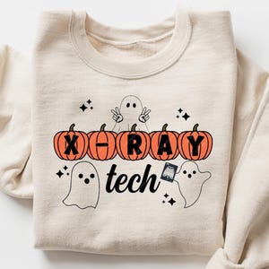 Puede incluir: Sudadera color crema con un diseño temático de Halloween. El gráfico incluye calabazas naranjas, fantasmas y el texto "X-RAY tech". El diseño es en negro y naranja, perfecto para la temporada de sustos.