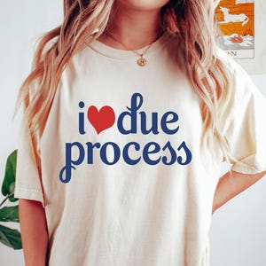 May include: A cream-coloured t-shirt featuring the text "I ❤️ due process" in blue script with a red heart. The t-shirt is a relaxed fit, ideal for casual wear.