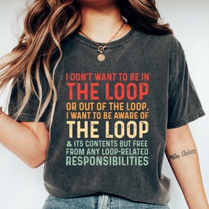 May include: Dark gray t-shirt with the text "I DON'T WANT TO BE IN THE LOOP" in red, yellow, and green. The shirt also includes the phrases "OR OUT OF THE LOOP. I WANT TO BE AWARE OF THE LOOP & ITS CONTENTS BUT FREE FROM ANY LOOP-RELATED RESPONSIBILITIES."