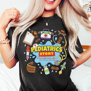 May include: A black t-shirt featuring a colorful graphic with the text PEDIATRICS STORY TO INFINITY AND BEYOND FOR OUR PATIENTS. The design includes medical icons like a stethoscope, bandages, a clipboard, a syringe, and a medical kit.