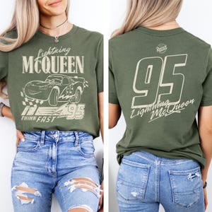 May include: Olive green t-shirt featuring Lightning McQueen from the Cars movie. The front graphic includes the character, the number 95, and the phrase "Think Fast." The back displays a large "95" and "Lightning McQueen" text.