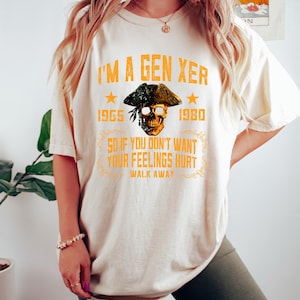 Puede incluir: Camiseta color crema con el texto "I'M A GEN XER" en naranja. El dise&ntilde;o incluye una calavera con sombrero de pirata, los a&ntilde;os 1965 y 1980, y la frase "SO IF YOU DON'T WANT YOUR FEELINGS HURT WALK AWAY."