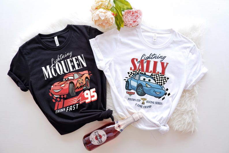 May include: Two t-shirts featuring Lightning McQueen and Sally Carrera from the Cars movie. One black shirt has McQueen with the text "Lightning McQueen 95 Think Fast." The other is white with Sally and the text "Lightning Sally Piston Cup Racing Series 1 Time Champ."