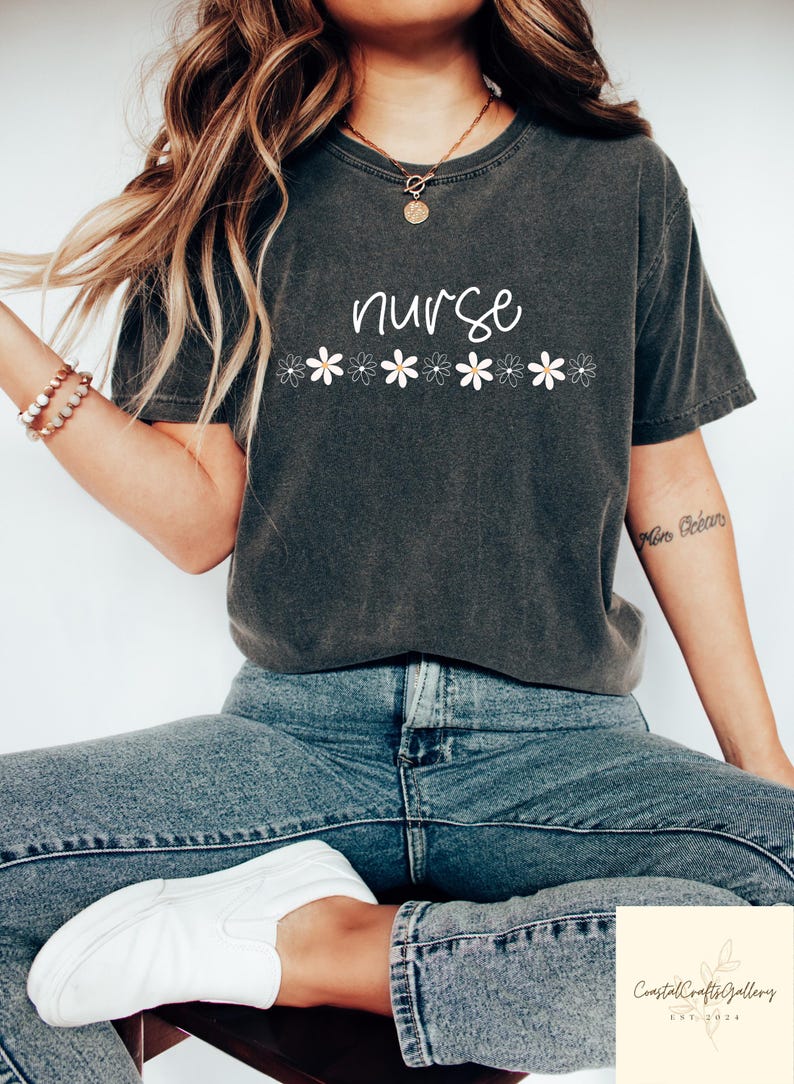 May include: Dark grey t-shirt with the word "nurse" in white script, above a row of white daisies. The shirt is worn with blue jeans and white trainers. A casual, comfortable style.