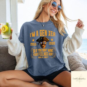 Puede incluir: Camiseta azul con el texto "I'M A GEN XER" y una calavera con un sombrero de pirata. La camiseta tambi&eacute;n incluye los a&ntilde;os 1965 y 1980, y la frase "SO IF YOU DON'T WANT YOUR FEELINGS HURT WALK AWAY."