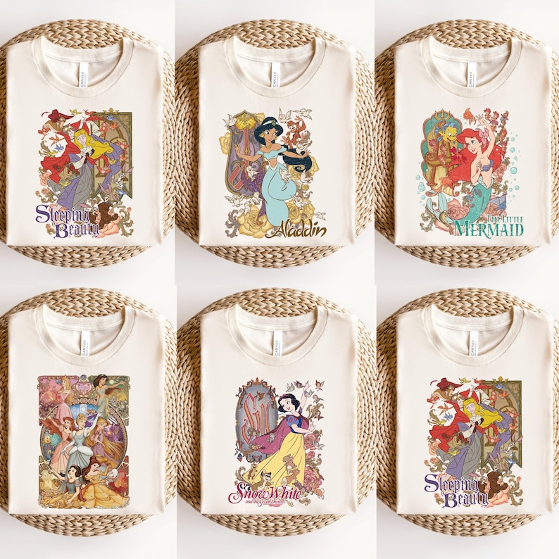 May include: A collection of six cream-coloured t-shirts, each featuring a different graphic print of a classic animated character. The designs include Sleeping Beauty, Aladdin, The Little Mermaid, a group of princesses, and Snow White with floral motifs.
