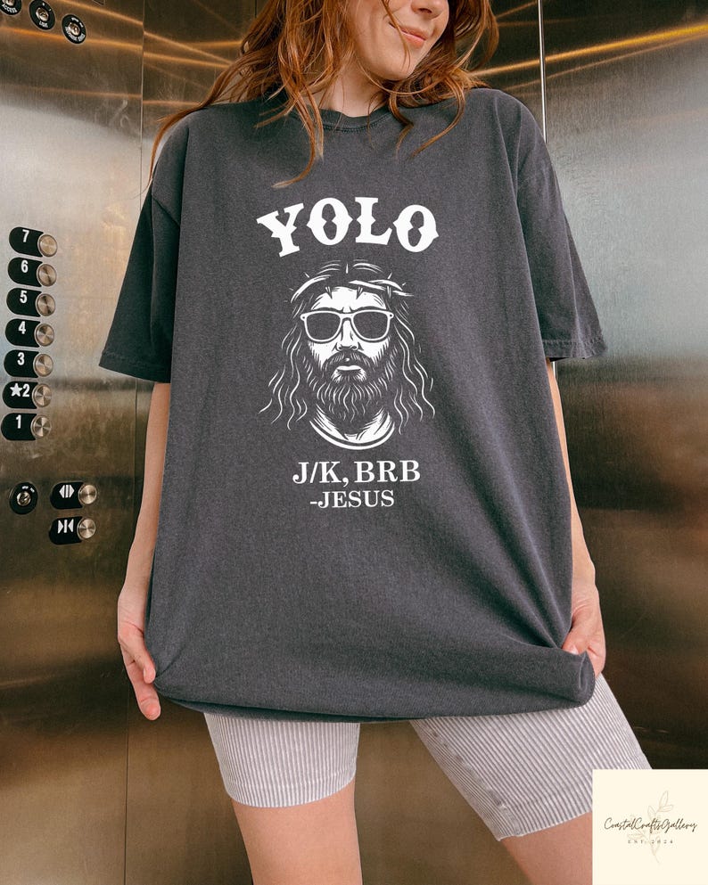Peut inclure: T-shirt gris fonc&eacute; avec le mot "YOLO" au-dessus d'un dessin de J&eacute;sus portant des lunettes de soleil et une couronne d'&eacute;pines. Le texte "J/K, BRB - JESUS" est en dessous. Le t-shirt est de style d&eacute;contract&eacute;.