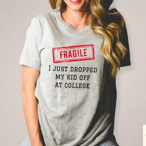 May include: A light gray t-shirt with the text "FRAGILE" in a red rectangle, and the text "I JUST DROPPED MY KID OFF AT COLLEGE" in black. The shirt is short-sleeved.