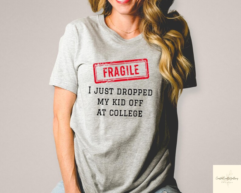 May include: A light gray t-shirt with the text "FRAGILE" in a red rectangle, and the text "I JUST DROPPED MY KID OFF AT COLLEGE" in black. The shirt is short-sleeved.