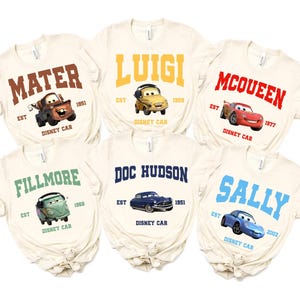 May include: Six off-white t-shirts featuring Disney Cars characters. Each shirt displays a character's name in bold letters, along with an image of the car and the text "Disney Car". The characters include Mater, Luigi, McQueen, Fillmore, Doc Hudson, and Sally.