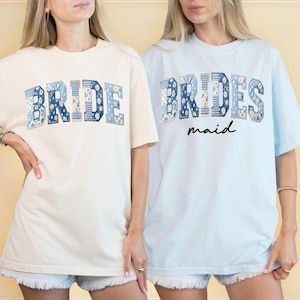 Puede incluir: Dos camisetas, una crema y otra azul claro, con texto. La camiseta crema dice "BRIDE" en letras de patchwork azules. La camiseta azul claro dice "BRIDES" encima de "maid" en escritura negra, con letras de patchwork azules.