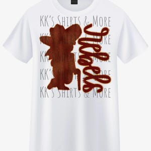 Może przedstawiać: Biała koszulka z brązową grafiką przedstawiającą osobę i słowem "Whee" w kursywie. Tekst "KK'S SHIRTS & MORE" jest wydrukowany jasnoszarą czcionką na koszulce.