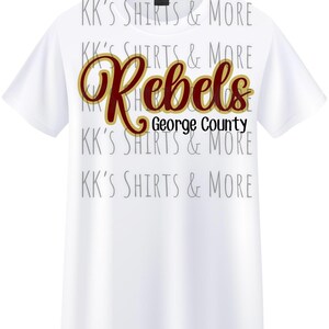 Puede incluir: Camiseta blanca con la palabra "Rebels" en escritura granate y dorada, con "George County" debajo en negro. La camiseta también tiene el texto "KK'S SHIRTS & MORE" repetido en un patrón gris descolorido.
