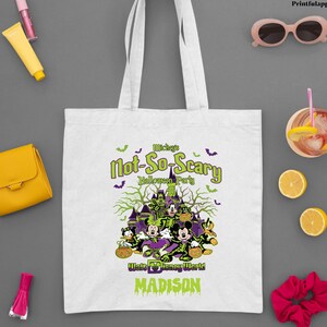 May include: White tote bag featuring a Halloween design with Mickey Mouse and friends. The text reads "Mickey's Not-So-Scary Halloween Party" with "Walt Disney World" and "Madison" below. Includes a logo for Printfulapparelus.