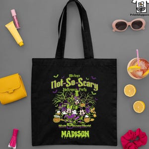 May include: Black tote bag featuring a Halloween design with Mickey Mouse and friends. The bag has the text "Mickey's Not-So-Scary Halloween Party" and "Walt Disney World" with the name "Madison" below. Other items include sunglasses, a wallet, and a drink.