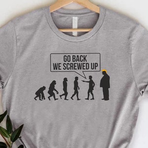 May include: A gray t-shirt with a black and white illustration of the evolution of humans. The last human in the illustration is wearing a yellow hat and is saying "Go back we screwed up".