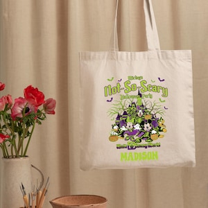 May include: Beige tote bag featuring a Halloween design with Mickey Mouse and friends. The bag has the text "Mickey's Not-So-Scary Halloween Party" and "Walt Disney World MADISON" in green and purple.