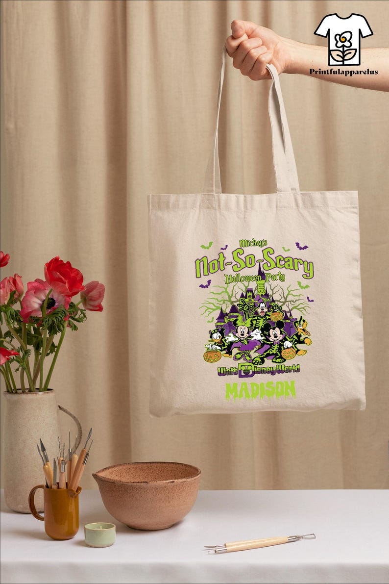 May include: Beige tote bag featuring a Halloween design with Mickey Mouse and friends. The bag has the text "Mickey's Not-So-Scary Halloween Party" and "Walt Disney World MADISON" in green and purple.