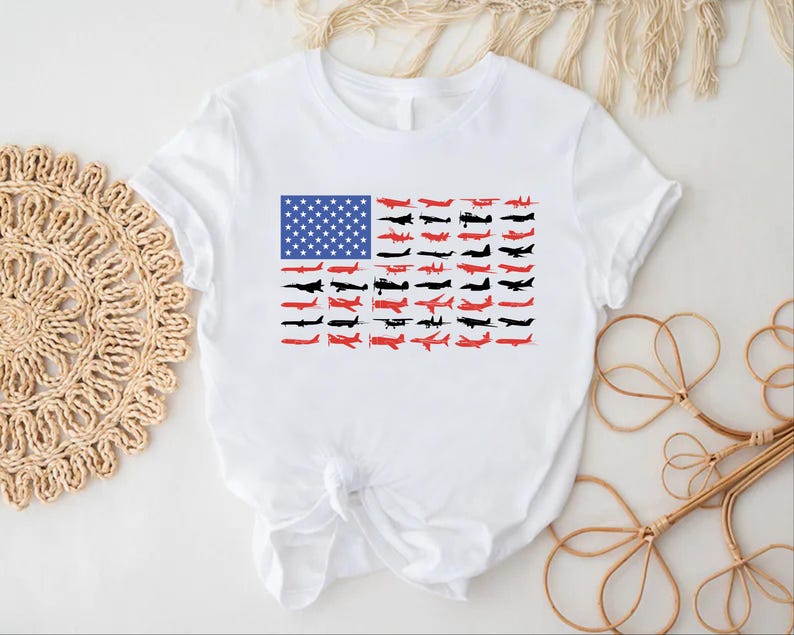 Peut inclure: T-shirt blanc avec un motif du drapeau am&eacute;ricain compos&eacute; d'avions. Le motif du drapeau comprend un rectangle bleu avec des &eacute;toiles blanches et des rang&eacute;es de silhouettes d'avions rouges et noires.