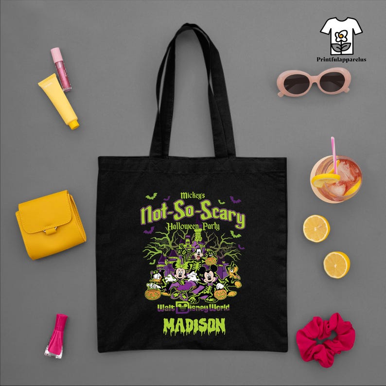 May include: Black tote bag featuring a Halloween design with Mickey Mouse and friends. The bag has the text "Mickey's Not-So-Scary Halloween Party" and "Walt Disney World" with the name "Madison" below. Other items include sunglasses, a wallet, and a drink.
