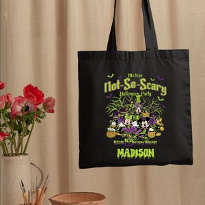 May include: Black tote bag featuring a Halloween design with Mickey Mouse, Donald Duck, and Goofy. The text reads "Mickey's Not-So-Scary Halloween Party" and "Walt Disney World" in green and purple. The name "Madison" is also displayed.