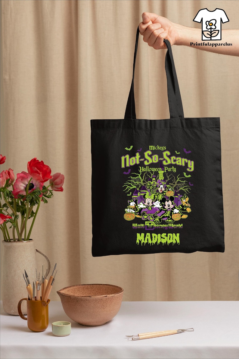 May include: Black tote bag featuring a Halloween design with Mickey Mouse, Donald Duck, and Goofy. The text reads "Mickey's Not-So-Scary Halloween Party" and "Walt Disney World" in green and purple. The name "Madison" is also displayed.