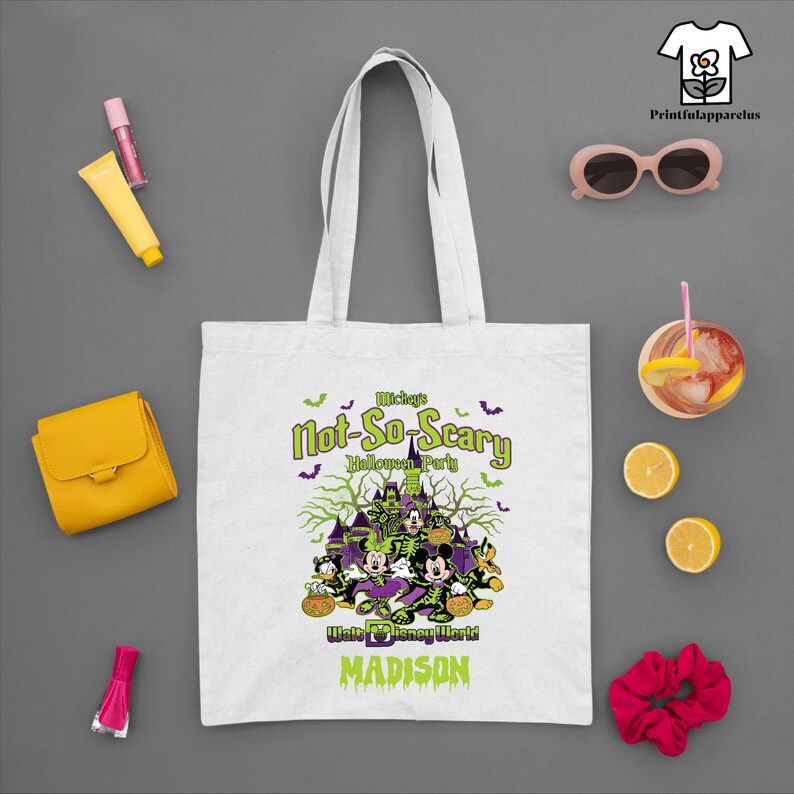 May include: White tote bag featuring a Halloween design with Mickey Mouse and friends. The text reads "Mickey's Not-So-Scary Halloween Party" with "Walt Disney World" and "Madison" below. Includes a logo for Printfulapparelus.